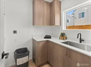 The laundry area blends functionality and style with full cabinetry, durable quartz counters, and a deep utility sink.
