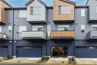 The back of the townhome with the garage entrance, balcony/deck, and a modest gardening area