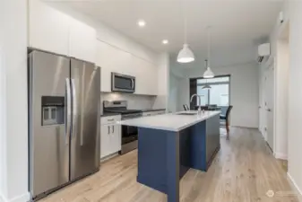 Ultra-modern kitchen features a quartz island and counters, stainless appliances and a gas cooktop.  There is spot and can lighting, and vinyl plank flooring.  Notice also the Mitsubishi Mini-Split HVAC