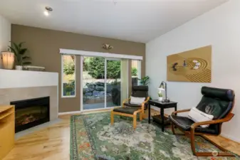 a  living room with a cozy fireplace & slider that leads to a private patio, which faces a green belt