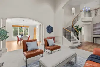 Light-filled formal living room with soaring ceilings, graceful staircase, and expansive windows creating an impressive first impression.