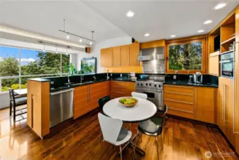 A circular breakfast table gathers light from walls of glass, making every meal feel like dining in the park. Walnut cabinetry and high-end appliances complete a kitchen where daily life flows with ease and connection to nature.