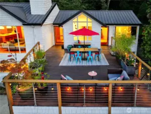 The dining and living rooms spill naturally onto an elevated deck, extending the home’s heart into the open air. Here, meals and gatherings take on a parkland backdrop, where Olmsted’s woodland and evening sky become part of the setting.