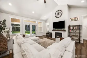 Family Room with vaulted ceiling gas fireplace (propane fueled). French doors lead to the backyard, doorway left of fireplace leads to primary suite, doorway to right of fireplace leads to one of the additional bedrooms and a full bathroom.