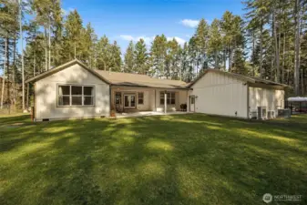 Back of home is very private, fully-fenced and surrounded by towering evergreen trees providing abundant privacy. Window on left side of home is primary suite, center is the covered patio & French doors to family room, window to right is the dining nook, garage is to the right. Also note: next to the heat pumps is an installed generator.
