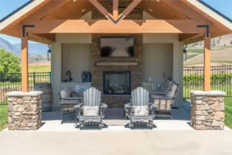 Covered pool lounge area equipped with a sink, beverage coolers, TV and propane fireplace