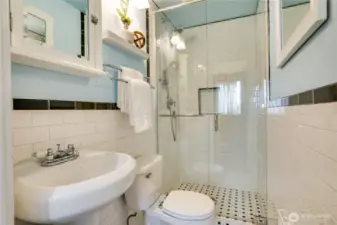 Classic tile enhances this main floor guest bathroom, featuring floor-to-ceiling shower tile behind a glass door, a pedestal sink, and a handy medicine cabinet.
