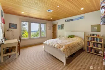 Comfortable guest bedroom with large windows, natural light, and peaceful wooded surroundings.