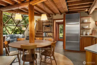 At the heart of the home, the central dome reveals an open kitchen with a built-in dining table. Geometric dome windows blur the line between indoors and out, immersing you in the surrounding forest.