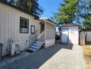 Side parking area with gravel and cement area, shed in back.