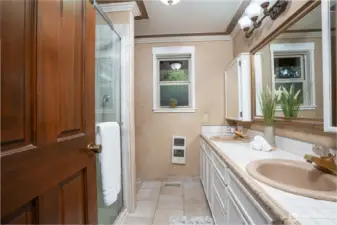 Well-appointed bathroom featuring a spacious double vanity with ample storage, classic tile countertops, and a large mirror for added functionality. A glass-enclosed shower offers convenience, while warm tones and natural light create a comfortable, inviting space for daily routines.