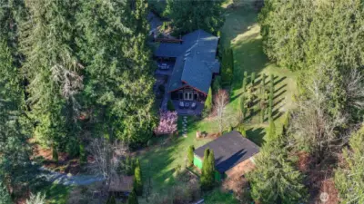 Aerial view showcasing the full beauty and privacy of the property, surrounded by mature evergreens and open usable land. The home is perfectly positioned to take advantage of the serene setting, with expansive yard space, landscaped grounds, and additional outbuildings offering versatility for hobbies, storage, or workspace. A true Pacific Northwest retreat with room to live, grow, and enjoy.
