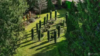 Beautifully designed garden space featuring structured plantings and trellis frames, creating a unique and serene outdoor focal point. Surrounded by mature evergreens, this private setting offers endless potential for gardening, relaxation, or outdoor gatherings.