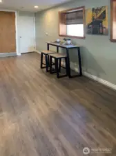 This area of the lower level is being used as the dining area. The space is large enough to hold a more traditional table. The white door in the back of the photo is a spacious pantry. The wood door on the left side of this photo is the interior access to the main floor.