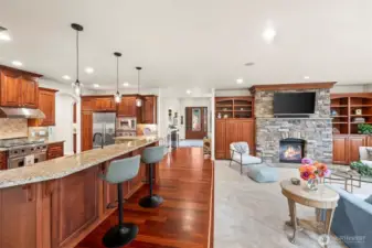 Expansive great room blending living, kitchen, and dining, anchored by rich hardwoods, custom cabinetry, and a floor-to-ceiling stone fireplace.