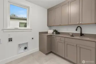Well appointed laundry room with custom cabinets, slab counters, and stainless steel sink
