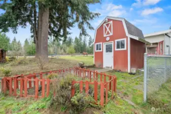 Storage shed and water tank area featuring ample loft storage, shelving for gardening tools, and a fenced herb garden.