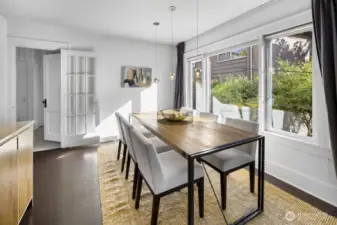 Bright dining room with triple windows to lush landscaping; glass door maintains light between rooms.