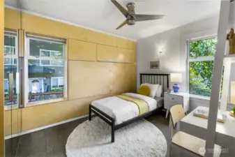 Flexible bedroom/office with warm paneling, desk zone, and leafy outlooks on two sides.