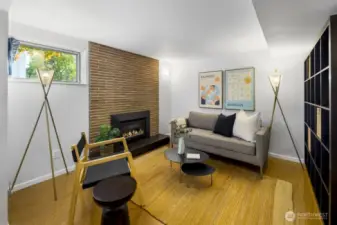Cozy lower-level studio lounge/TV room featuring a brick-accent gas fireplace and durable flooring.
