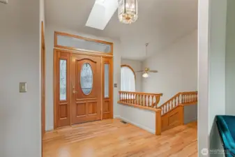 Step into a warm and welcoming foyer filled with natural light from a skylight above, highlighting true oak hardwood floors and elegant millwork.