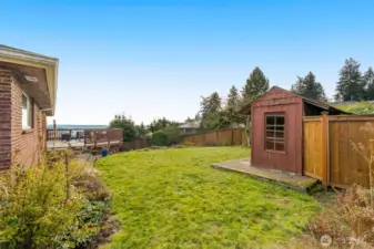 Grassy fenced backyard for play, separate lower patio area, potting shed