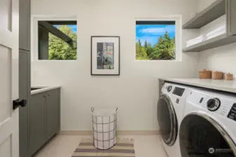 Upper level laundry has washer and dryer, floating shelves, cabinet storage and laundry sink.
