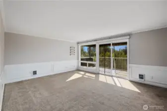 Living Room: Light-filled living room with large windows and sliding glass doors that open to the covered balcony. Neutral finishes, crown molding, and treetop views create a comfortable, inviting retreat.