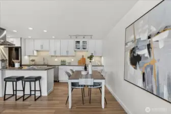 The open dining area sits perfectly next to the chef's kitchen and living space, creating an effortless flow for everyday meals and entertaining alike. Warm new LVP floors, under-cabinet lighting, and the crisp white cabinetry with mosaic tile backsplash set an elevated yet welcoming tone — while the generous dining space easily accommodates a full table.