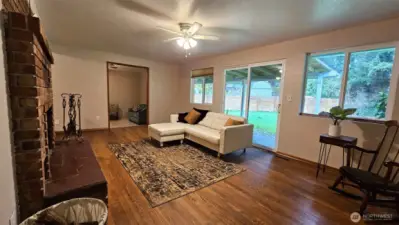 View from the hallway to the family room with hardwood floors, slider to the backyard, ceiling fan, and brick fireplace. Notice the doorway to one of the bonus rooms on the far wall.