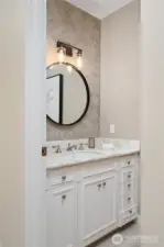 Main level powder room features antique cabinetry, marble counter top, pewter faucet, and hexagon accent tile.