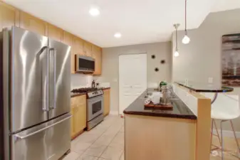 Kitchen including SS appliances, gas stove, bar top seating, and tucked away washer/dryer.