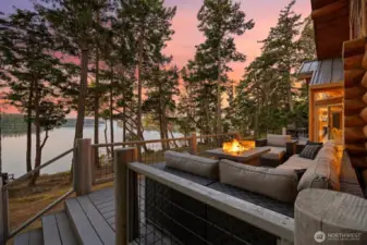 Enjoy serene evenings on the expansive deck surrounded by towering evergreens. A perfect space for gathering, all set against a stunning waterfront backdrop and glowing sunset skies.