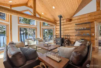 Living room with soaring ceilings and expansive windows floods the space with light and offers uninterrupted views of the water, framed by hand-hewn log beams.