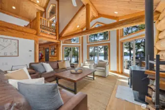 Sunlit great room boasts exposed log architecture and towering view windows, creating an inviting space for relaxation and entertaining against a stunning natural backdrop.