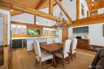 Elegant dining area with high beamed ceilings and luxe lighting, seamlessly flowing into the gourmet kitchen and offering views of the lush natural surroundings.
