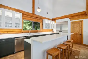 High-end stainless steel appliances, dual prep sinks, and expansive stone countertops make this a chef’s dream, complemented by views of the ocean framed by handcrafted log detail.