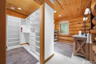A thoughtfully designed primary closet and dressing area connects to the bathroom with generous built-in shelving, drawers, and hanging storage — all tucked beneath pine ceilings and adjacent to the log-lined vanity.