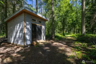 A charming forest shed offers ample storage for tools, kayaks, or recreational gear. Adjacent trails weave through the wooded acreage, perfect for nature walks and peaceful exploration.