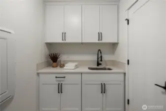Laundry Room: Bright and functional laundry space with upper and lower cabinetry, quartz counters, and a deep sink for easy cleanup. The washer and dryer hookup is ready for your appliances, and extra storage keeps everything organized.  Staged photos are of the model home of the same floorplan within the Foxmoore community and are for visualization purposes only. Colors, finishes, and layout can and will vary.