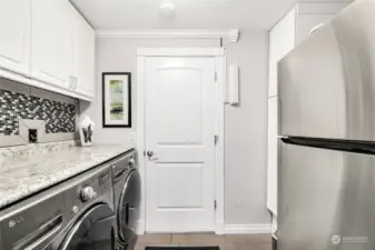 Laundry Room with entrance door to garage  Folding counter with tile backsplash  Upper cabinets and storage cupboard  Under cabinet lighting  Washer and dryer  Tile floors