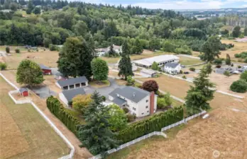 Back corner view showing house hidden behind arbevidous trees, 3 car & 4 car garages west end of home, driveway winds down to red 10 car garage & takes a right leading to barn & arena. Tacoma in top right of picture