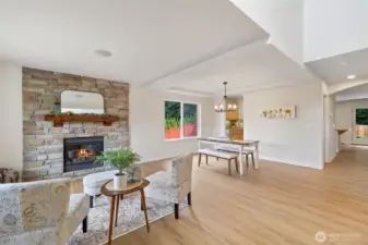 Vaulted entry into a well lit living and dining room with gas fireplace set in a Stone wall with mantel.