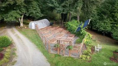Fenced garden with sixteen raised beds & green house. Not visible but on the property are two in-ground water storage tanks, two below ground owned propane tanks and one above ground propane tank. Solar panels on the roof of the home and a 6KW generator system.