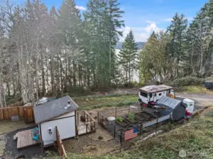 Off-grid 144 sq ft tiny home with wood-burning stove, set on a level pad and surrounded by fenced, oversized raised garden beds. Ideal basecamp for camping, homesteading, or future build plans.
