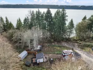 Aerial view showing the full 1-acre hillside layout with multiple leveled areas, established driveway access, cleared pads, and forested surroundings. Property backs directly to DNR land for added privacy.