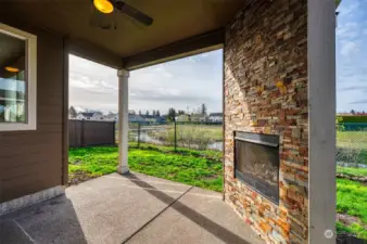 Enjoy outdoor living with this covered patio featuring a gas fireplace with slate backsplash, ceiling fan, fenced yard with open space to view.