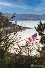 From your upland perch above Caledonia Cove, this is the scene that greets you—an American flag catching the sea breeze, the lighthouse standing watch, and the tide tracing its path along the curve of Browns Point. It’s a living landscape, where every hour brings a new expression of sky, water, and wonder.