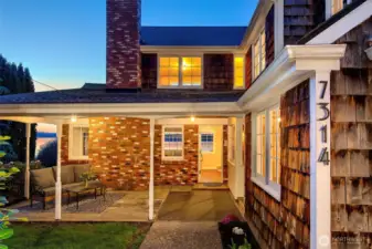 Under the soft glow of porch lights and the deepening hues of dusk, the entry to this Caledonia Cove Cape Cod radiates warmth and character. Weathered shingles, classic brickwork, and the home's original charm set the tone for what lies within—a peaceful upland sanctuary with panoramic views, timeless design, and a place in Browns Point history.