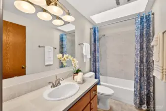 Full hall bath with a tiled tub surround, skylight, and an extended vanity counter for daily convenience. A great layout for shared use, with good light and easy functionality.